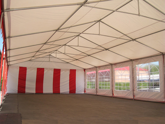 Wnętrze namiotu plenerowego z metalową konstrukcją i ścianami w biało-czerwone pasy oraz oknami, widok pustej przestrzeni przygotowanej na wydarzenie.
