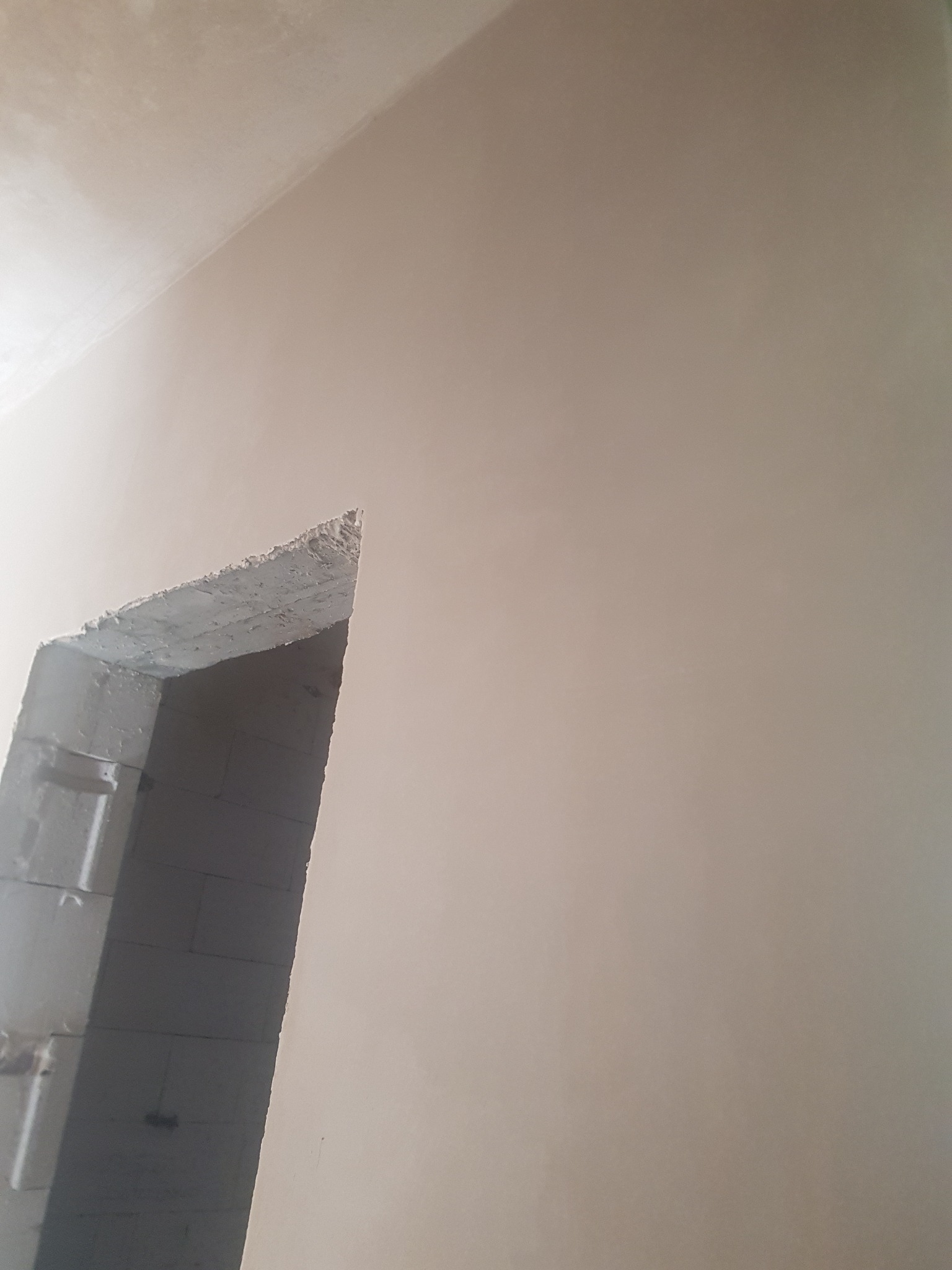 Ściana po nałożeniu gładzi, widoczny surowy otwór drzwiowy z bloczków, przygotowany do dalszych prac wykończeniowych.