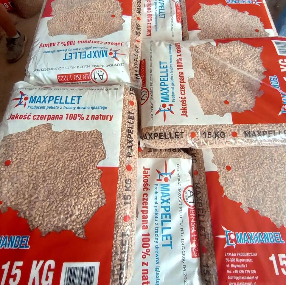 Stos worków 15 kg z pelletem drzewnym marki MAXPELLET, widoczne certyfikaty jakości i informacja o produkcji z trocin drewna iglastego.