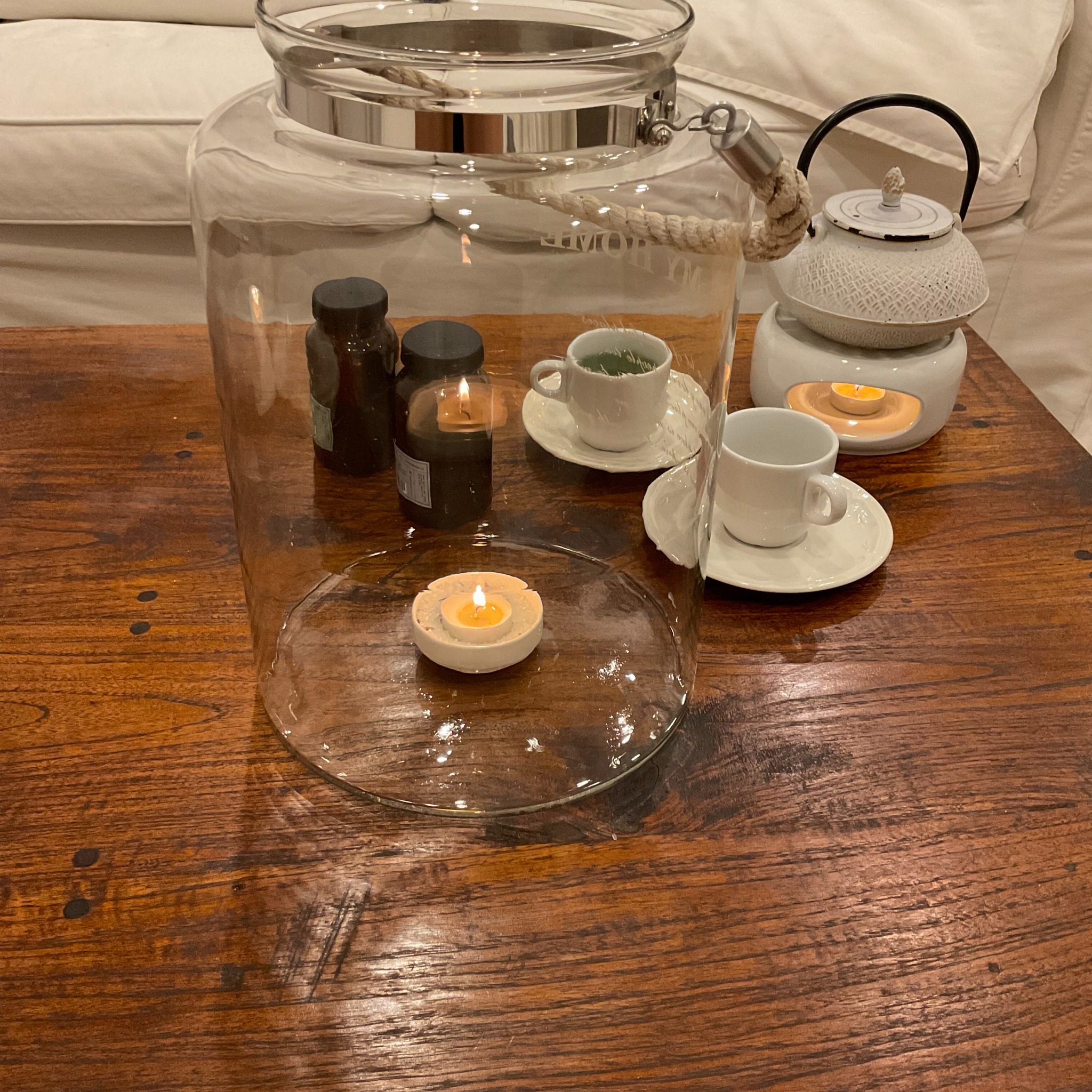 Szklany lampion z grubym sznurem, aromaterapia z ceramicznym czajnikiem i filiżankami na drewnianym stoliku kawowym w salonie.