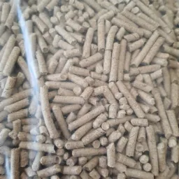 Bliski widok na brązowe, cylindryczne granulki w przezroczystym plastikowym worku, prawdopodobnie pellet drzewny, z widoczną fakturą i drobnymi pęknięciami na powierzchni.