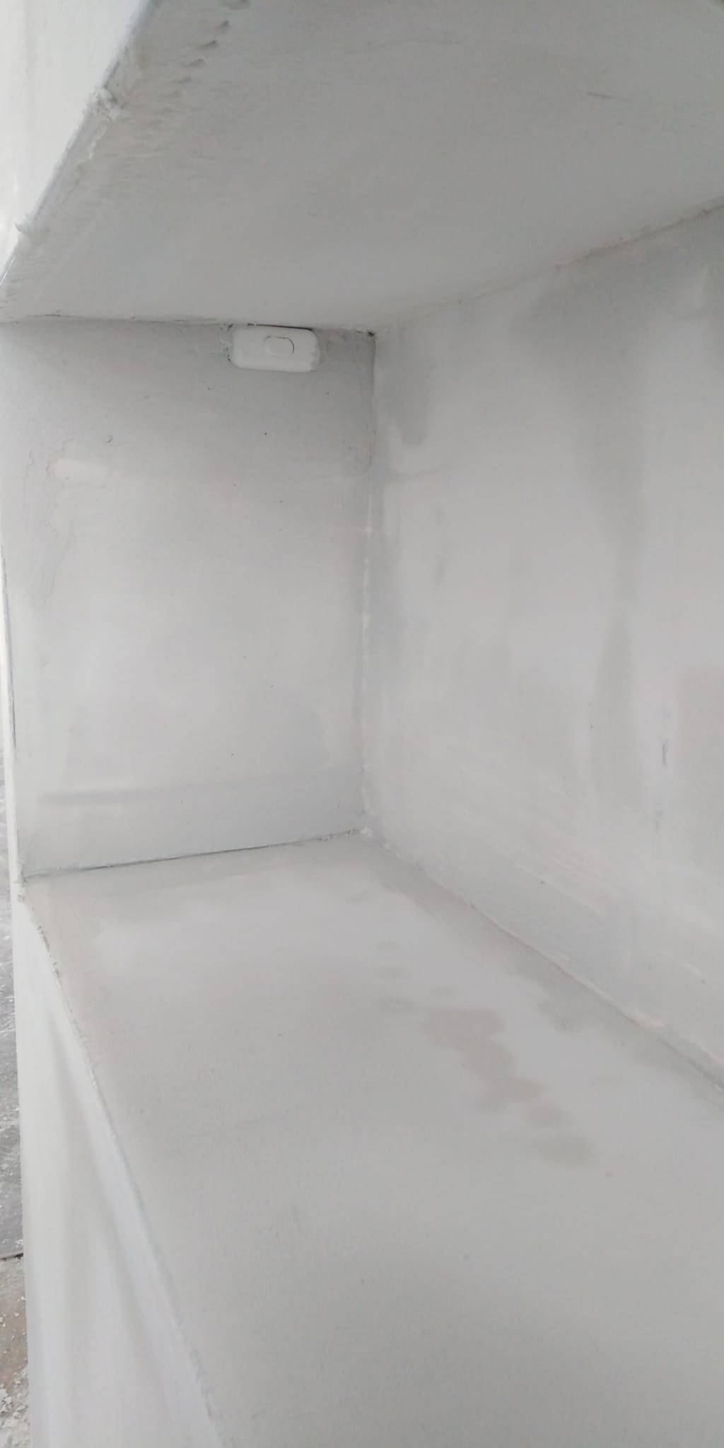 Wnętrze szafki lub wnęki pomalowane na biało, widoczny włącznik światła na górnej ścianie, świeża warstwa farby na ścianach i podłodze.