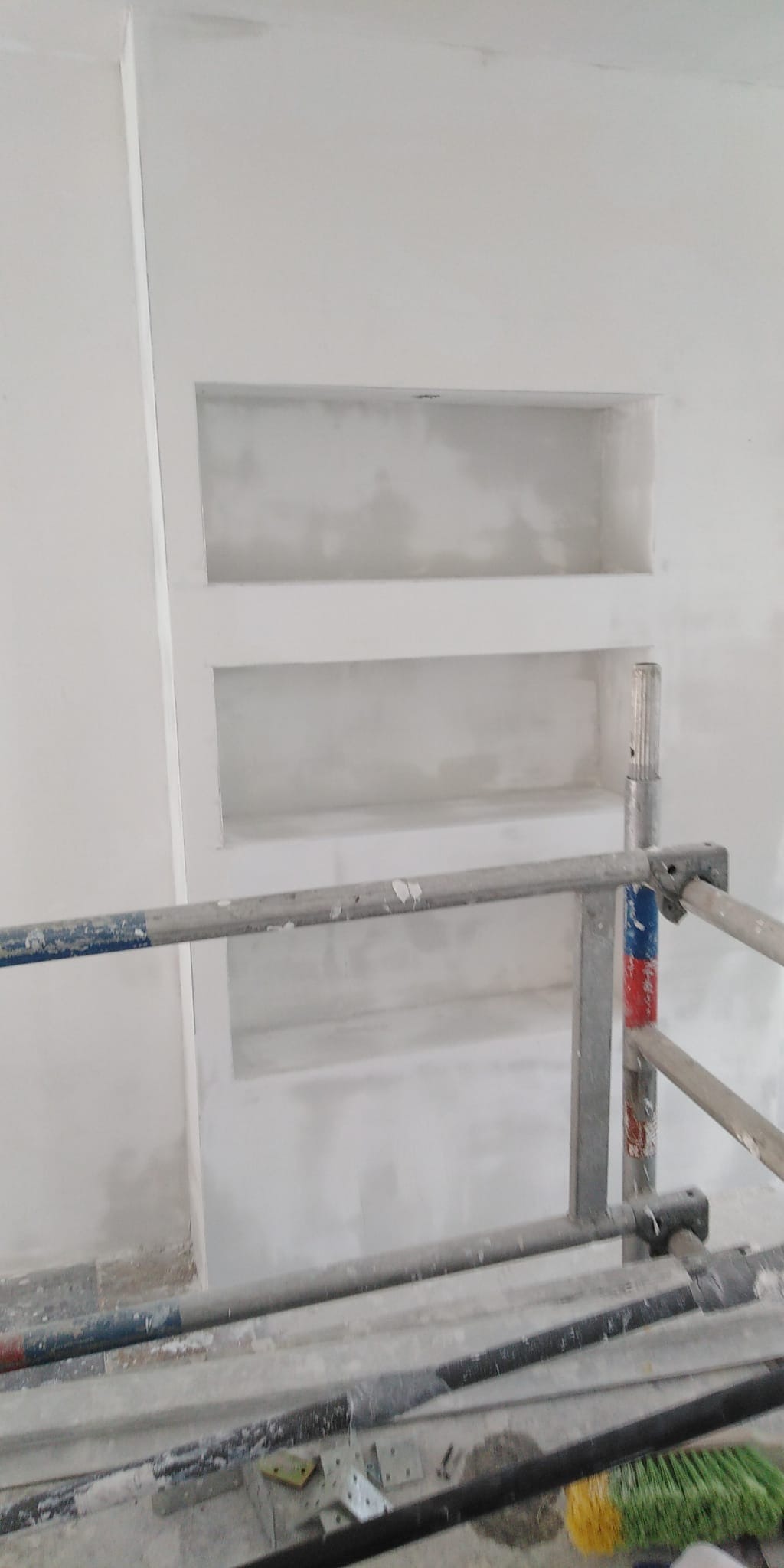 Wnęki w ścianie w trakcie szpachlowania, widoczne rusztowanie, surowy stan wykończenia.