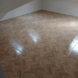 Ukończona podłoga z płytek o wzorze jodełki w pomieszczeniu ze skosami, widoczny fragment ściany i sufitu, jasne płytki z delikatnym rysunkiem drewna.