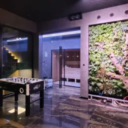 Nowoczesne wnętrze z pionową ścianą zieleni, szklaną sauną, marmurową podłogą i stołem do piłkarzyków.