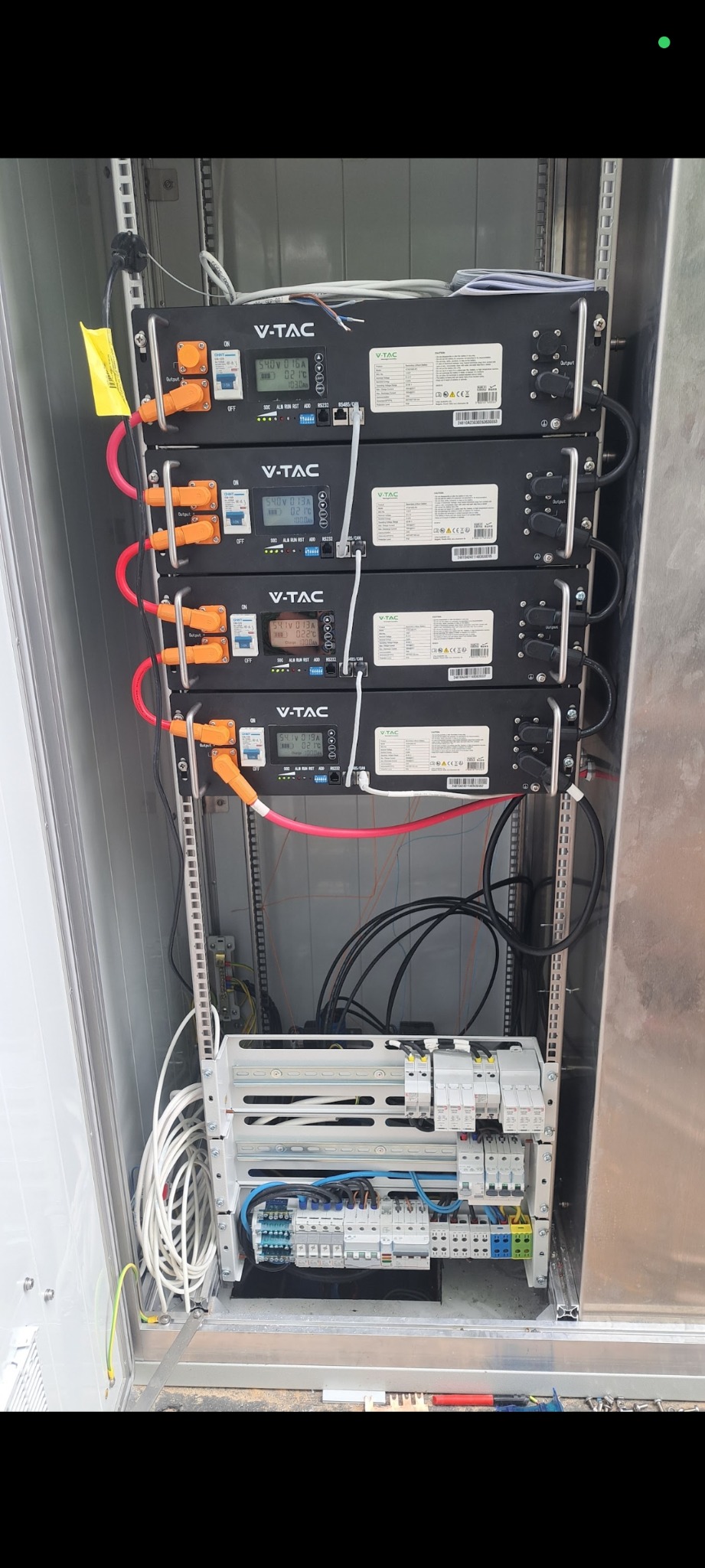 Szafa elektryczna z czterema modułami V-TAC, zabezpieczeniami i okablowaniem. Widoczne złącza, wyświetlacze, kable czerwone i czarne. Instalacja w szarej obudowie.