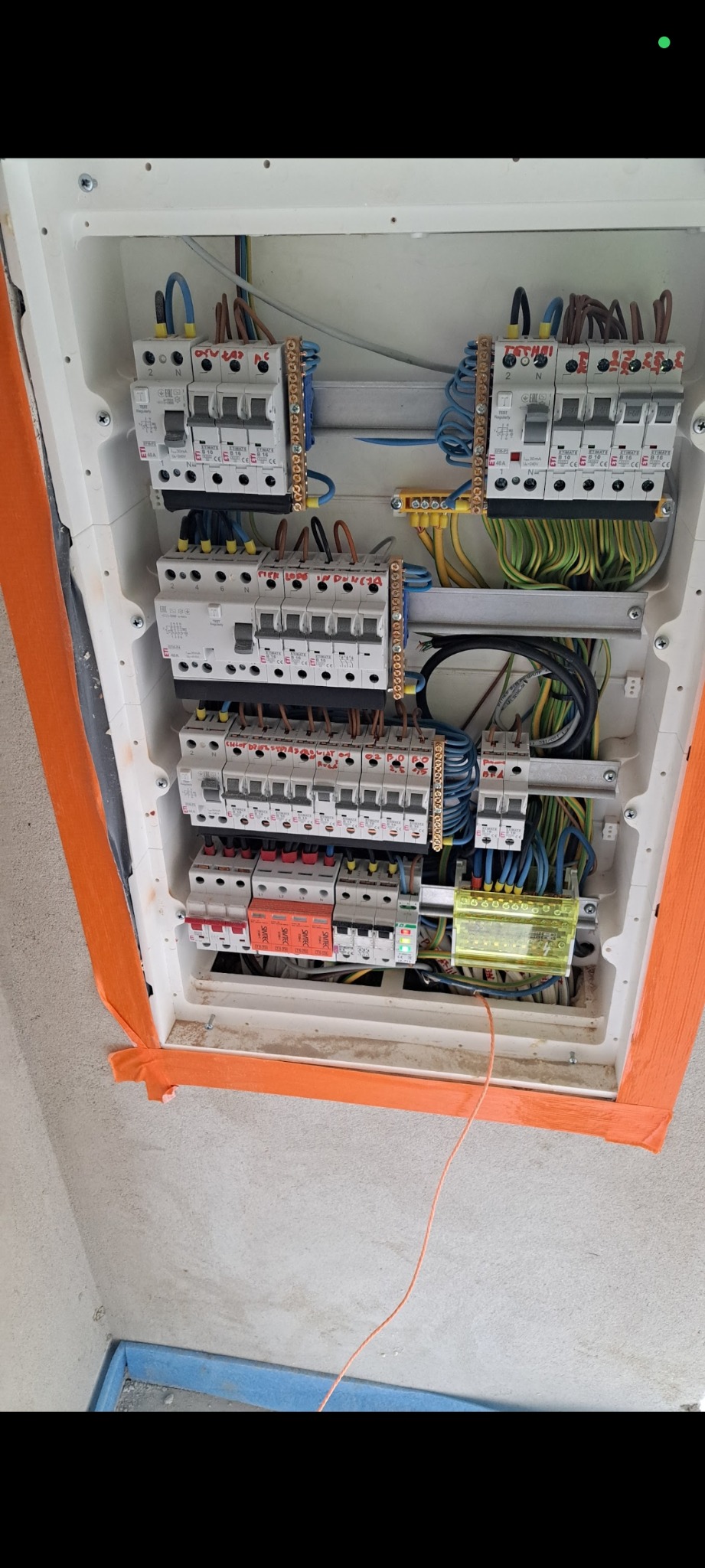 Rozdzielnica elektryczna z zabezpieczeniami, okablowaniem, i elementami montażowymi w białej obudowie, zabezpieczona taśmą malarską.