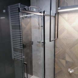 ArtDeco Łukasz Szatan - Nowoczesna kabina prysznicowa z czarnymi profilami i szklanymi drzwiami przesuwnymi, widoczna bateria prysznicowa i dekoracyjna płytka ścienna z geometrycznym wzorem.