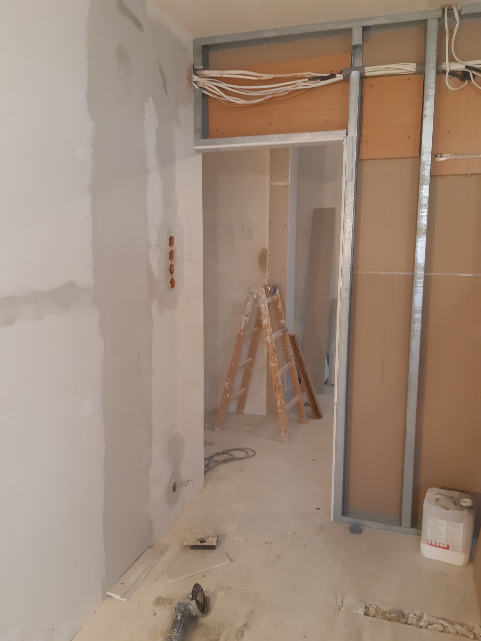 Wnętrze w trakcie prac wykończeniowych: ściana po szpachlowaniu, metalowa konstrukcja pod płytę karton-gips, drabina i widoczne przewody elektryczne.