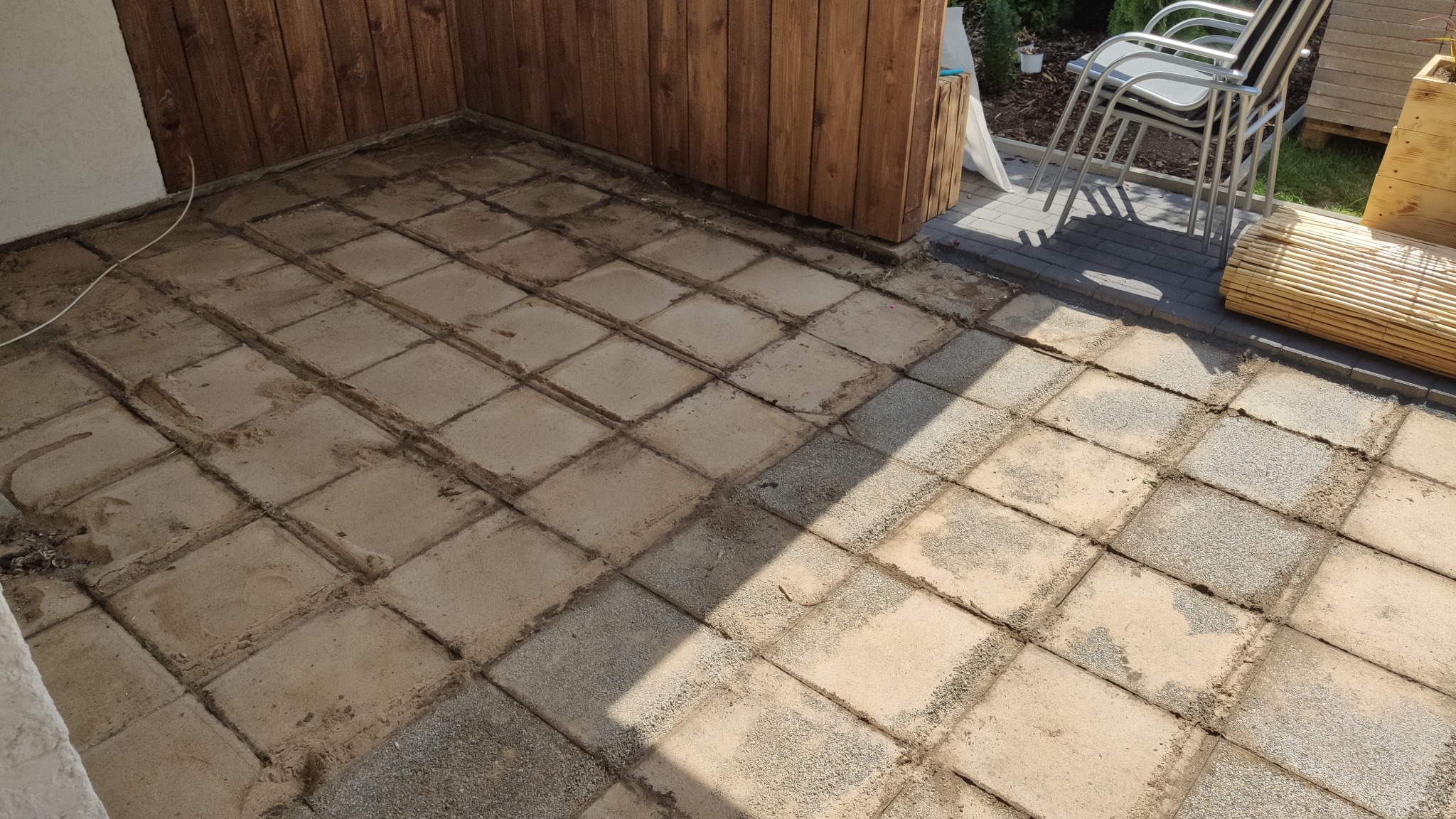 Przygotowanie podłoża pod taras z kostki brukowej, widoczne ślady po usuniętych płytach, drewniana ściana w tle.