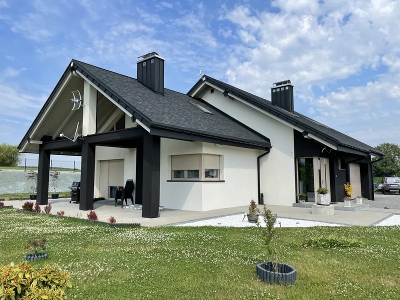 Nowoczesny dom jednorodzinny z białą elewacją i czarnymi elementami wykończeniowymi, widok z ogrodu na elewację frontową.