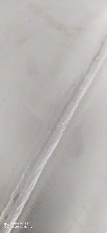 Zbliżenie na spoinę spawalniczą na metalowej powierzchni, widoczne ślady obróbki szlifierskiej.