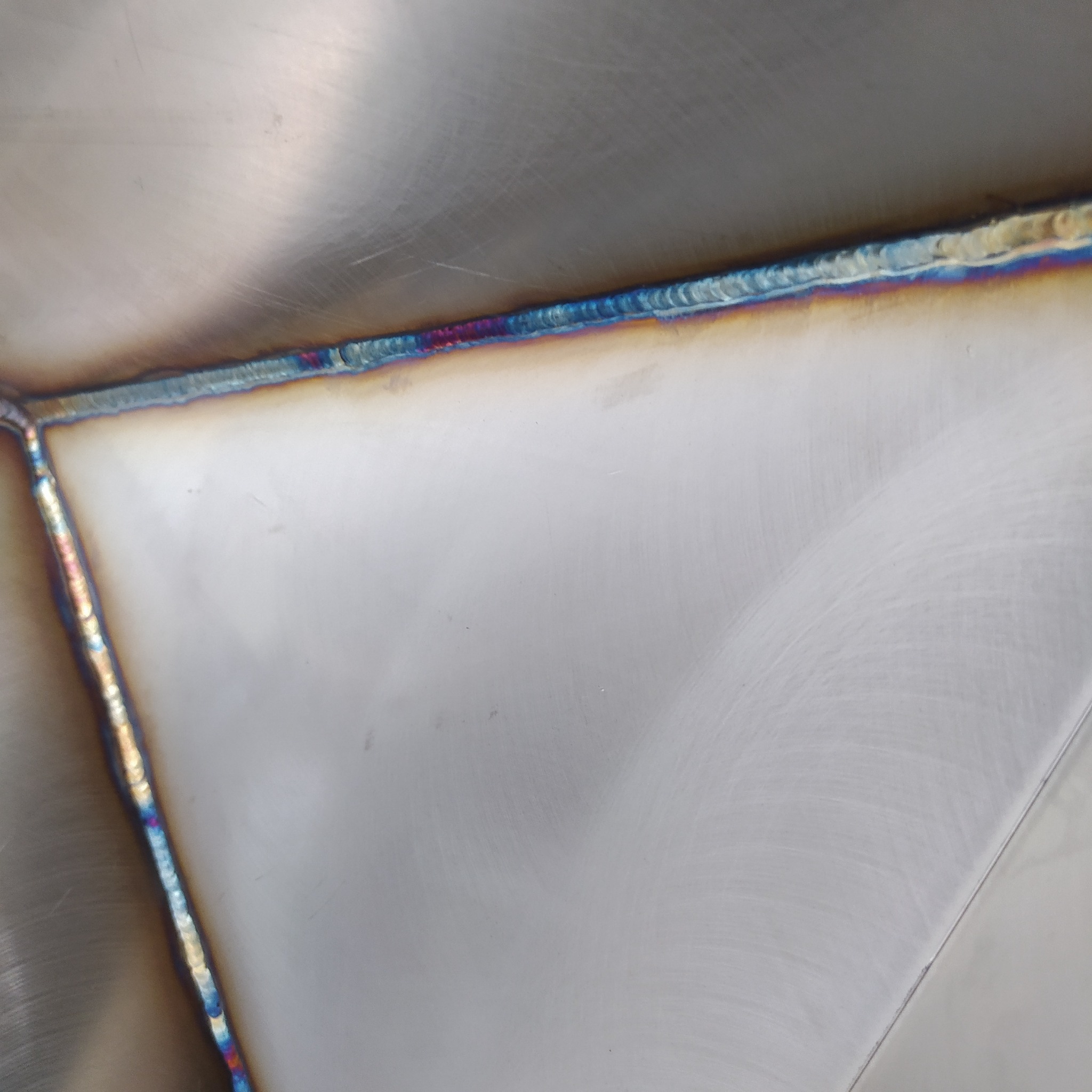 Szczegółowe zbliżenie na spoinę spawalniczą z widocznymi kolorami utleniania na powierzchni metalu.