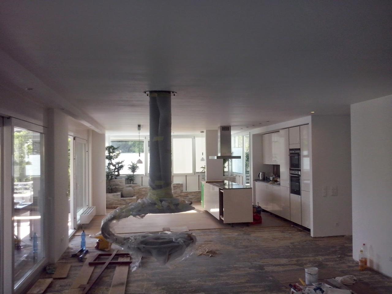 Wnętrze w trakcie prac wykończeniowych: zabezpieczony okap kuchenny, surowa podłoga, białe ściany i zabudowa kuchenna. Widoczne materiały i narzędzia.