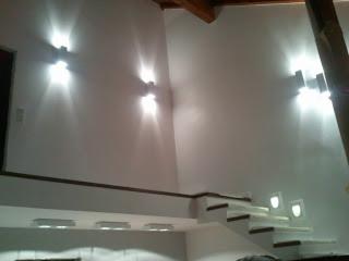 Białe schody ze zintegrowanym oświetleniem w nowoczesnym wnętrzu, oświetlone dodatkowo przez kinkiety ścienne. Widok z dołu, ukośne ujęcie.