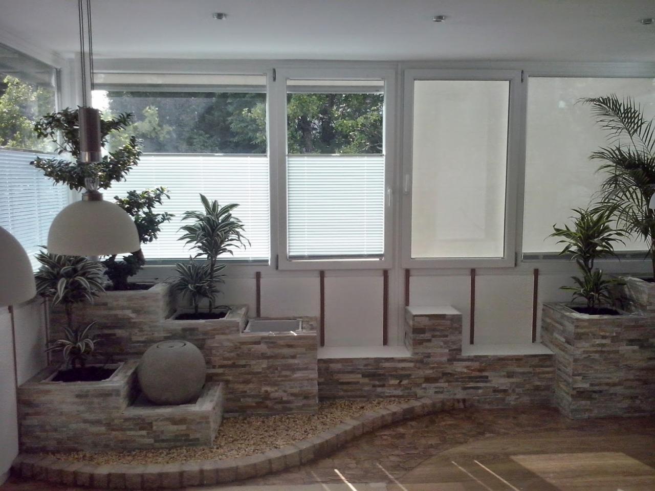 Aranżacja balkonu z kamiennymi donicami i roślinami, widok na okna z żaluzjami. Elementy dekoracyjne z kamienia i oświetlenie.