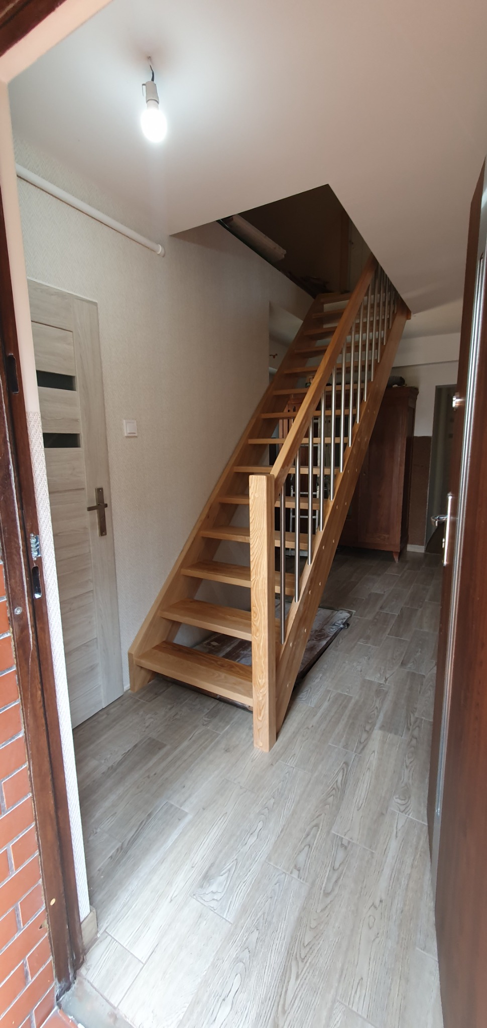 Jasne, proste schody z drewnianymi stopniami i metalową balustradą, prowadzące na wyższą kondygnację w jasnym wnętrzu.