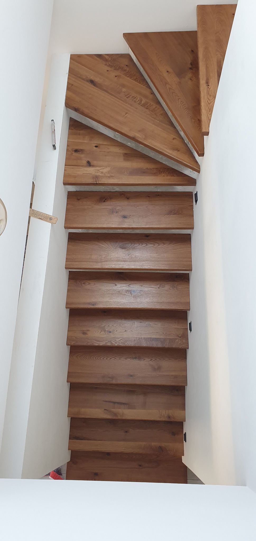 Widok z góry na drewniane schody o naturalnym wykończeniu, z widoczną strukturą drewna i minimalistycznym designem, osadzone w białym wnętrzu.