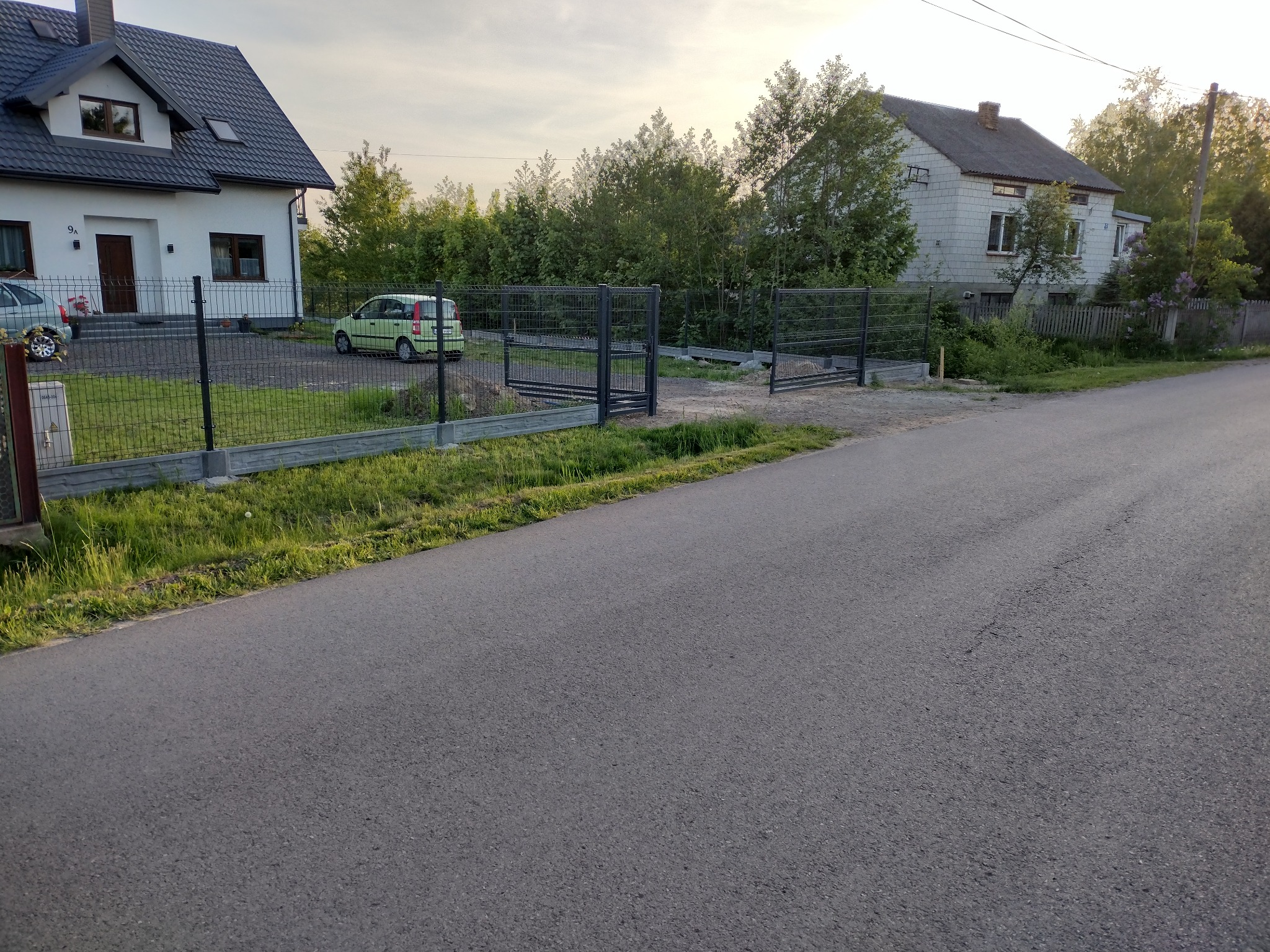 Nowoczesne, grafitowe ogrodzenie panelowe z podmurówką betonową i otwartą bramą wjazdową, widoczne z ulicy, z zielonym samochodem w tle.