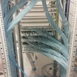 Uporządkowane, jasnoniebieskie kable sieciowe ułożone w metalowej szafie serwerowej z widocznymi punktami połączeń i elementami montażowymi.