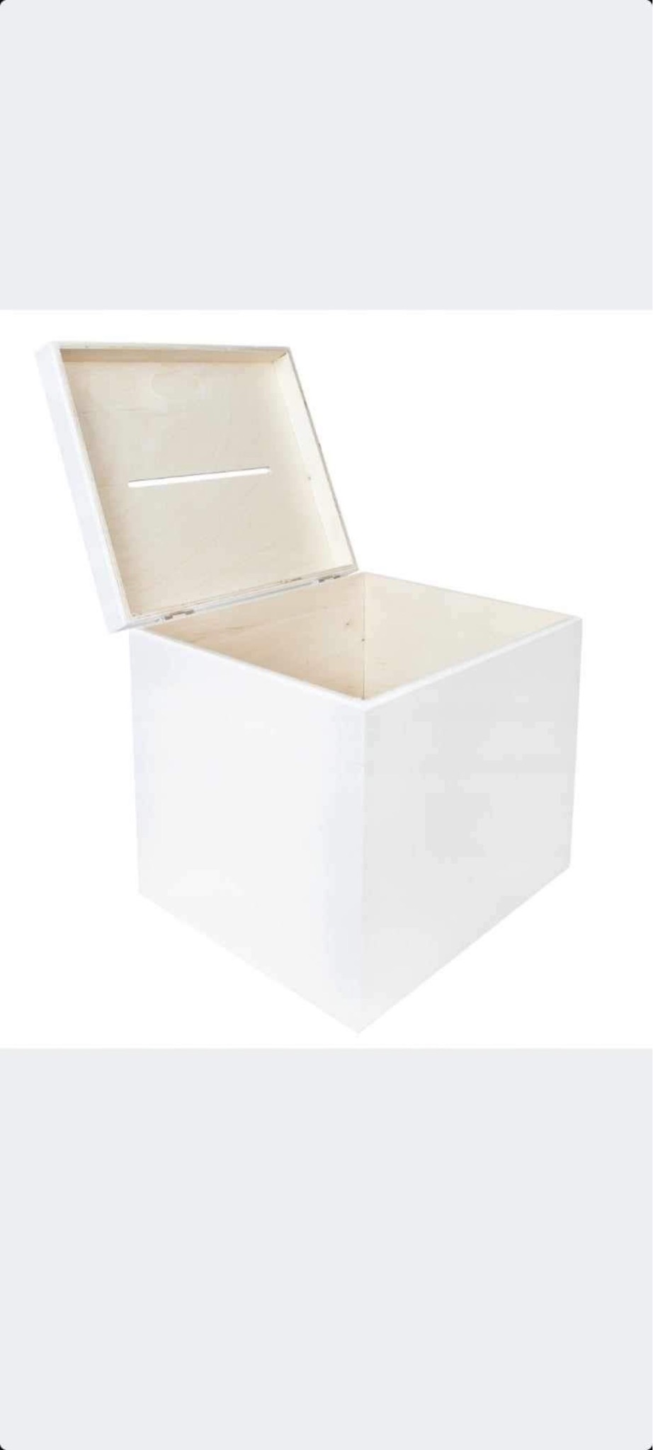 Białe, kwadratowe pudełko z drewna z uchylną pokrywą, w której wycięto szczelinę, ukazujące surowe drewno wewnątrz.
