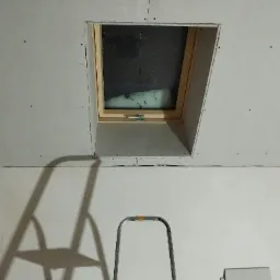 Montaż okna dachowego w ścianie z płyt gipsowo-kartonowych, widoczny fragment drabiny i niezagruntowane płyty