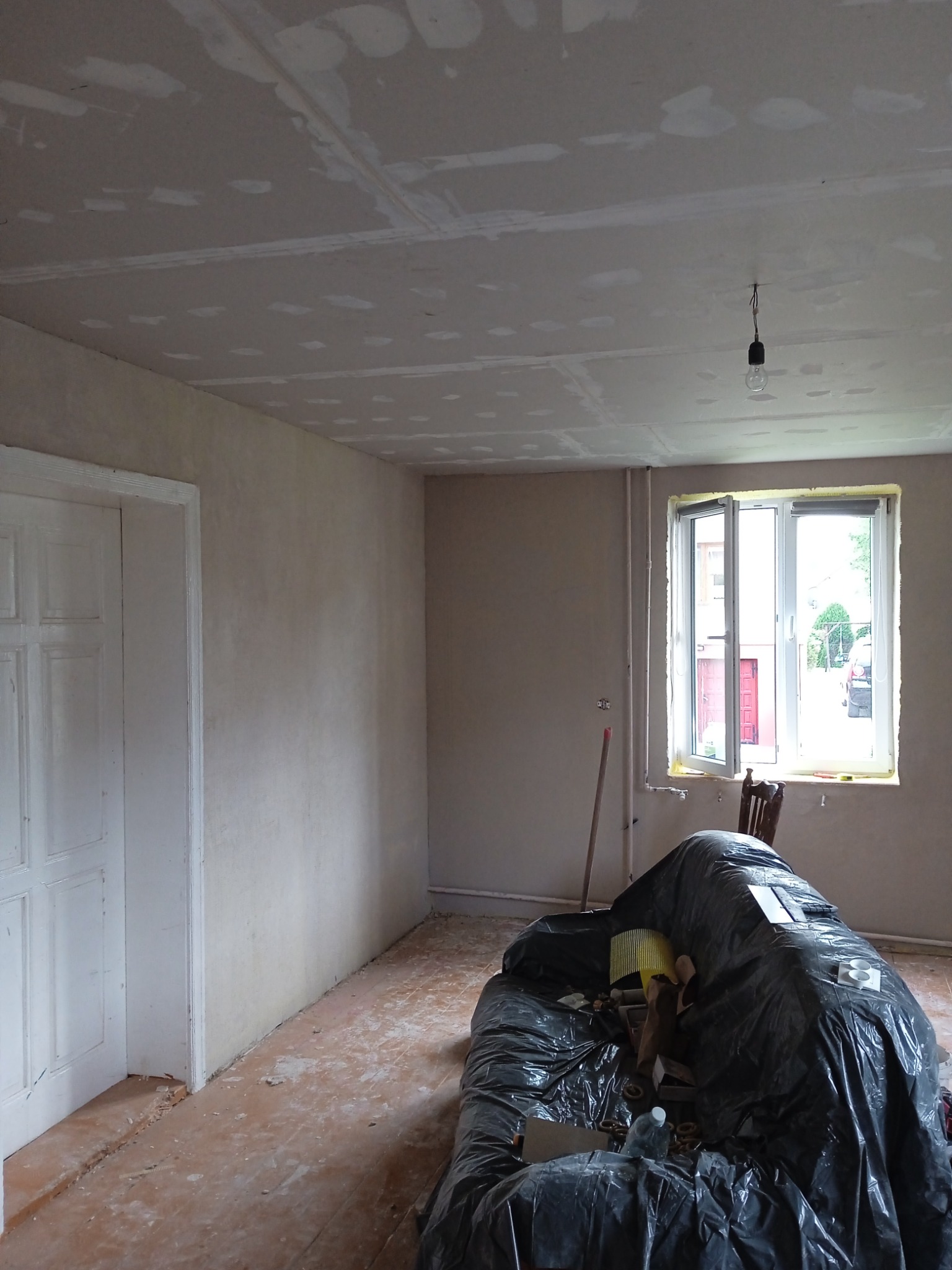 Pokój w trakcie remontu: ściany po szpachlowaniu, sufit z płyt kartonowo-gipsowych przed malowaniem, podłoga częściowo zabezpieczona folią, widoczne niedoskonałości powierzchni.