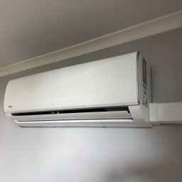 TECHCEL MARCEL ŻYDEK - Biały klimatyzator VIVAX zamontowany na szarej ścianie, widoczne przewody w białej maskownicy. Minimalistyczny design, nowoczesne rozwiązanie dla domu lub biura.