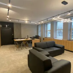 Nowoczesne wnętrze biura w Płocku z czarną sofą, drewnianym biurkiem i oświetleniem punktowym, widok na zimowy krajobraz za oknem.