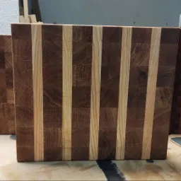 Trzy drewniane deski do krojenia z jasnymi i ciemnymi paskami ułożone obok siebie na warsztacie, widoczne ślady obróbki drewna.