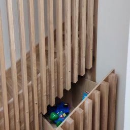 HIMEBLE SPÓŁKA Z OGRANICZONĄ ODPOWIEDZIALNOŚCIĄ - Drewniane schody z ażurową balustradą i wysuwaną szufladą na zabawki pod spodem, widoczny fragment podłogi z paneli.