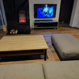 Nowoczesny salon z drewnianą podłogą, kominkiem z czarnego marmuru, telewizorem i stolikiem kawowym z jasnego drewna.