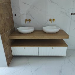 HIMEBLE SPÓŁKA Z OGRANICZONĄ ODPOWIEDZIALNOŚCIĄ - Nowoczesna łazienka z dwoma umywalkami nablatowymi, złotymi bateriami, drewnianym blatem i szafką z frezowanymi frontami na tle marmurowych płytek.