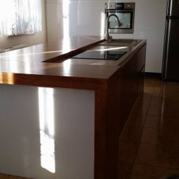 HIMEBLE SPÓŁKA Z OGRANICZONĄ ODPOWIEDZIALNOŚCIĄ - Nowoczesna kuchnia z białą zabudową i drewnianym blatem wyspowym z wbudowaną płytą grzewczą i zlewem, oświetlona naturalnym światłem wpadającym przez okno.