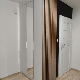 HIMEBLE SPÓŁKA Z OGRANICZONĄ ODPOWIEDZIALNOŚCIĄ - Nowoczesna szafa wnękowa z lustrzanymi drzwiami i dekoracyjnymi lamelami drewnianymi, umieszczona w jasnym wnętrzu obok białych drzwi.