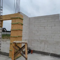 Wznoszenie ścian domu z bloczków, widoczne zbrojenie, szalunki z płyty OSB oraz podest roboczy.