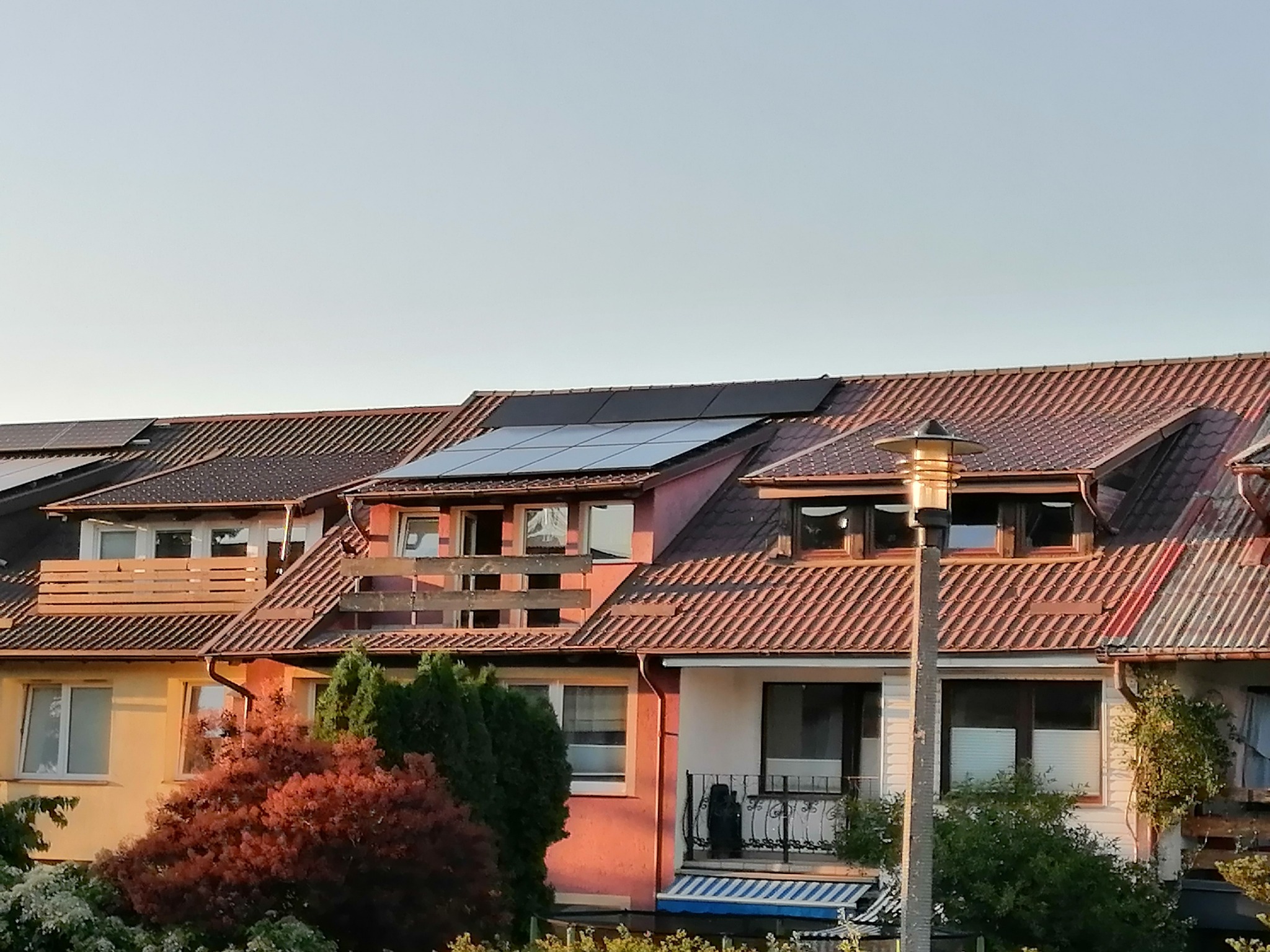 Rząd domów szeregowych z brązowymi dachówkami, na niektórych dachach panele słoneczne.