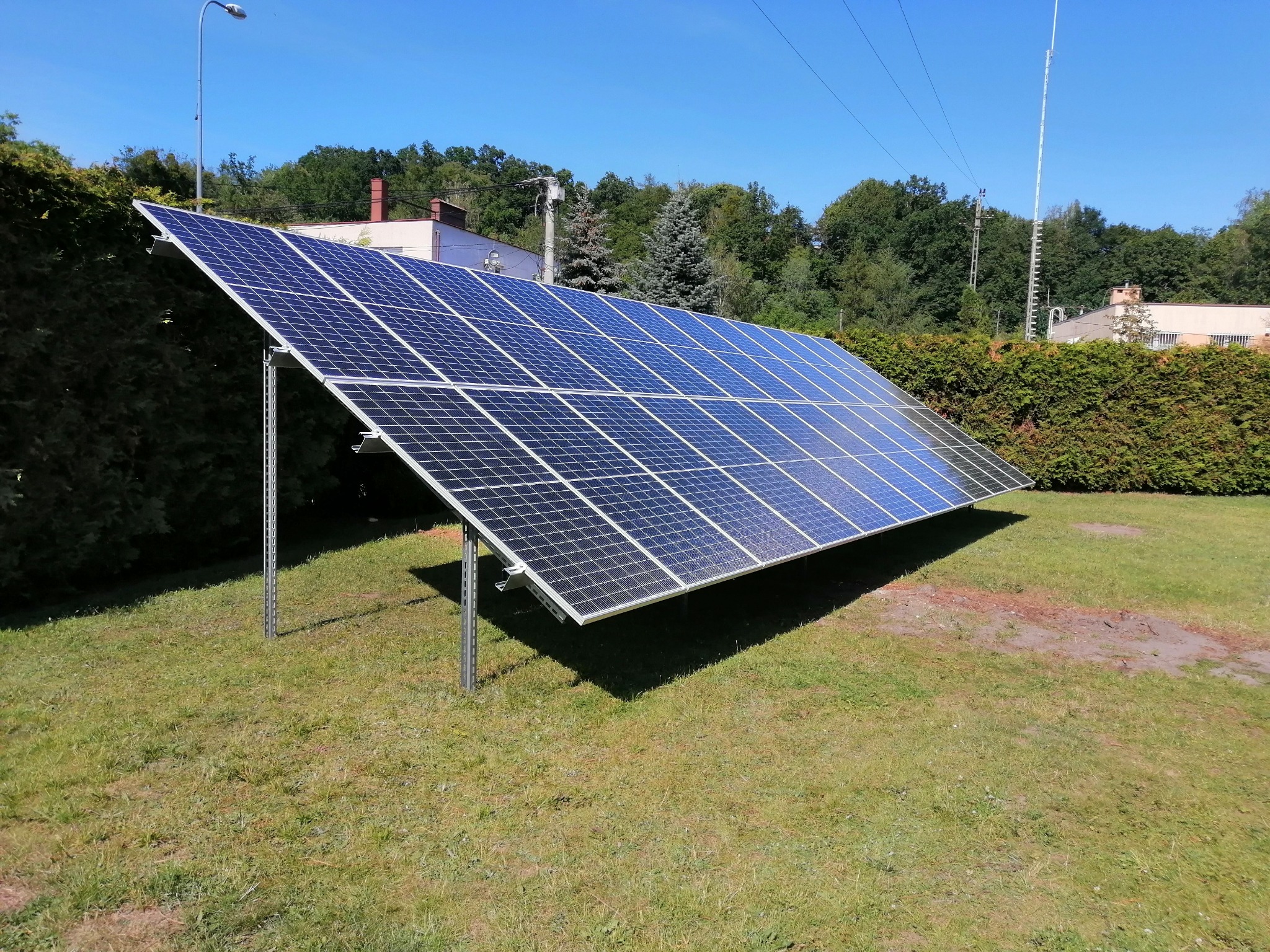 Panel słoneczny ustawiony na metalowych podporach na trawniku w słoneczny dzień.