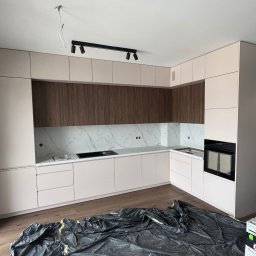 DAREKMEBLE Dariusz Głaz - Jasna kuchnia na wymiar z drewnianymi akcentami i marmurowym blatem, widok z perspektywy podłogi, zabezpieczonej folią malarską. Widoczne narzędzia.