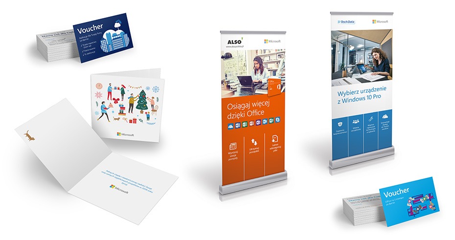 Zestaw materiałów reklamowych Microsoft: wizytówki, kartki świąteczne z motywem psa, roll-upy z hasłami reklamowymi Office i Windows 10 Pro, na białym tle.