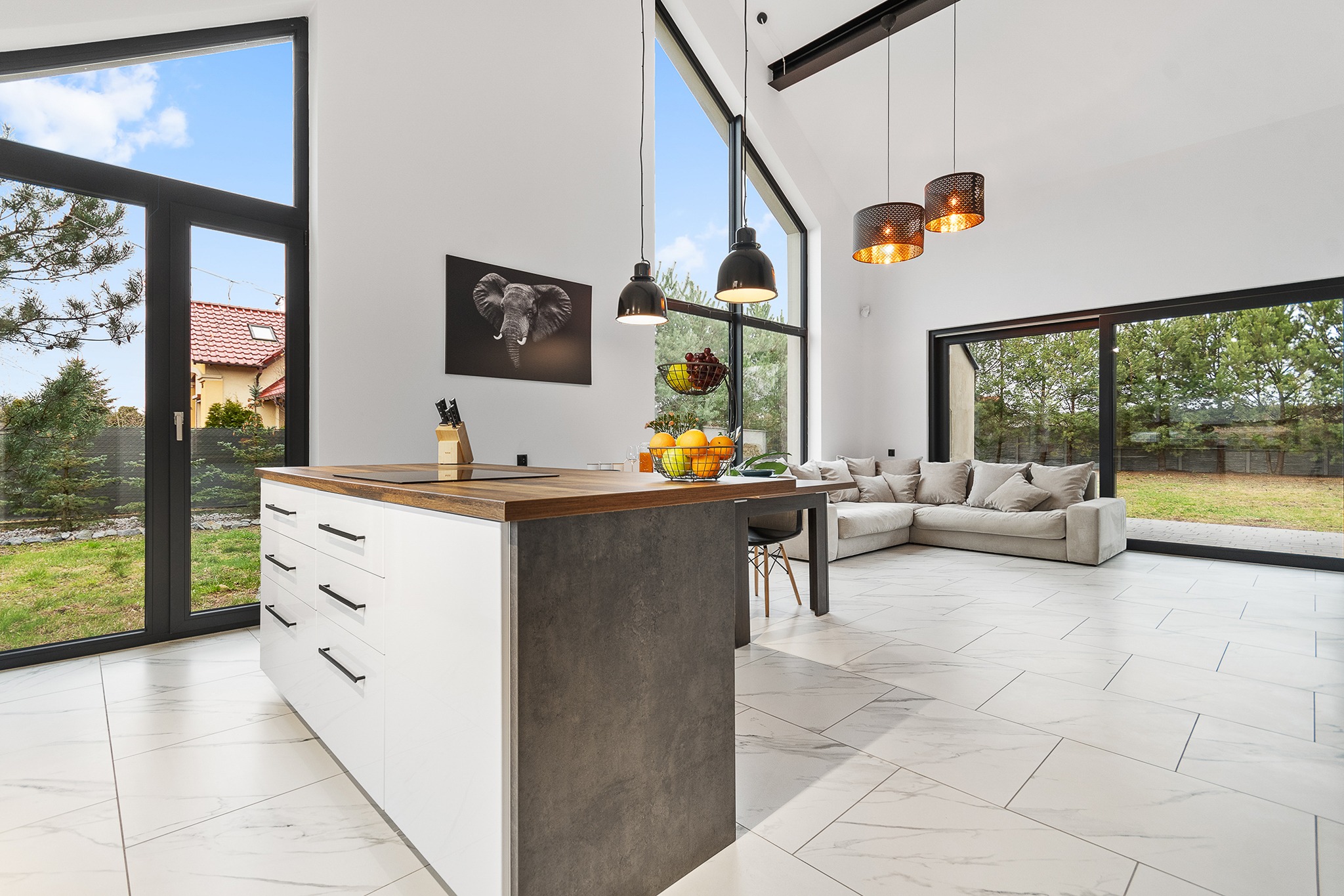 Jasna, nowoczesna kuchnia z wyspą i dużymi oknami, widok na ogród, podłoga z białego marmuru, minimalistyczny design.