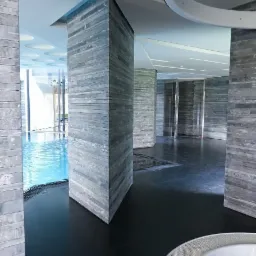 Wnętrze basenu z kolumnami obłożonymi szarym kamieniem łupanym, czarna podłoga, fragment wanny jacuzzi w prawym dolnym rogu.