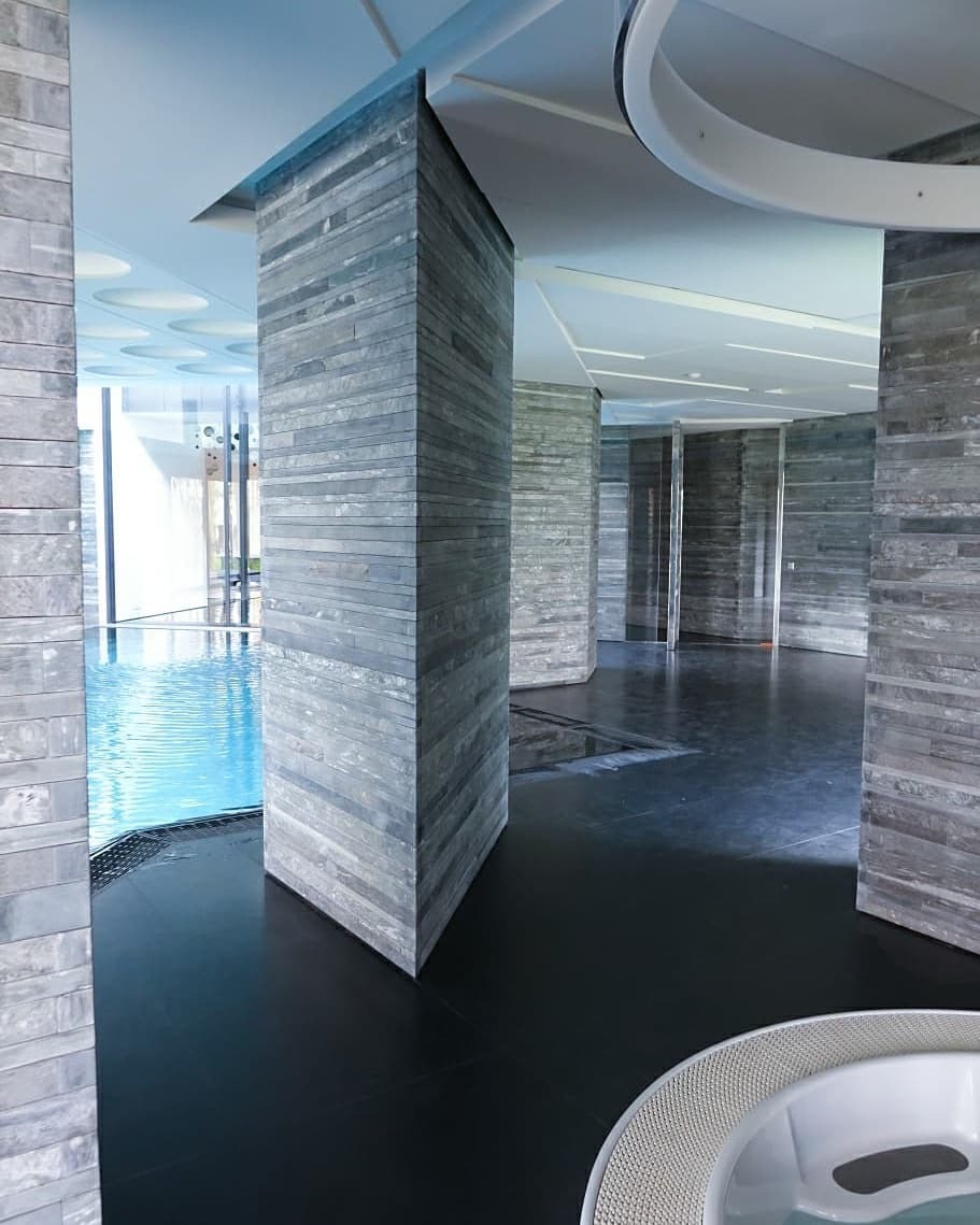 Wnętrze basenu z kolumnami obłożonymi szarym kamieniem łupanym, czarna podłoga, fragment wanny jacuzzi w prawym dolnym rogu.
