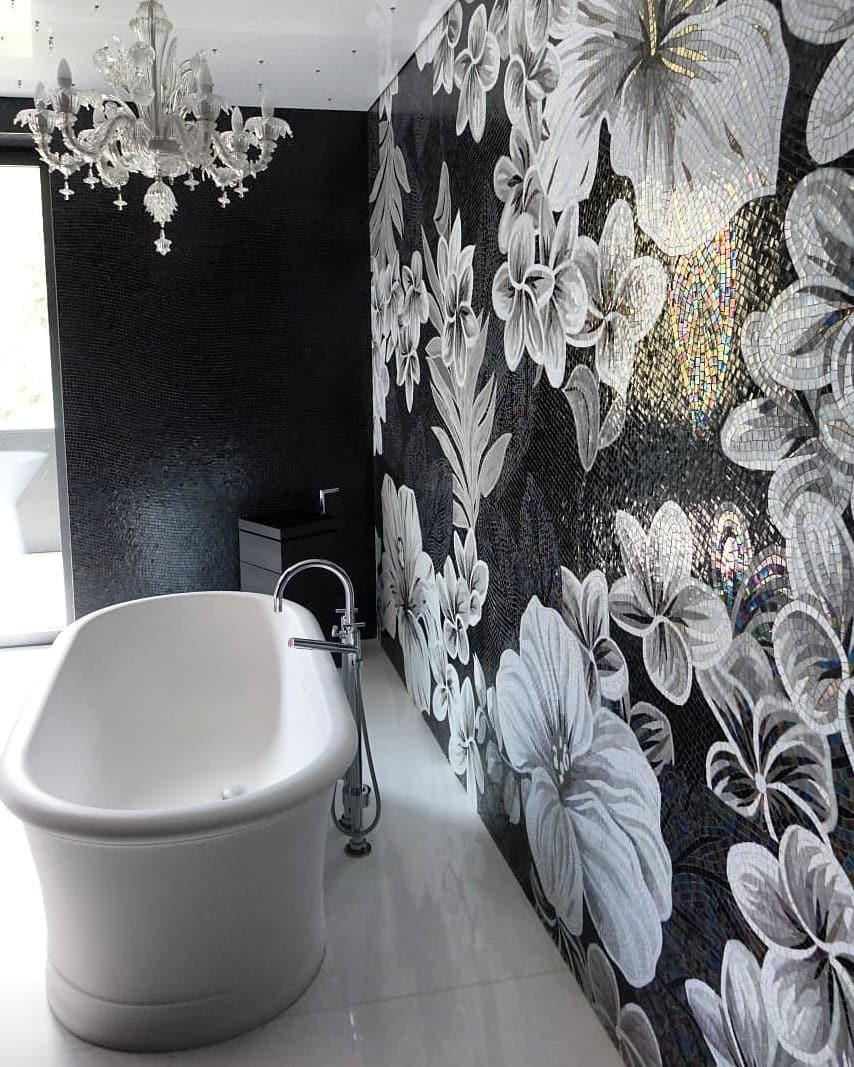 Elegancka łazienka z wolnostojącą białą wanną, mozaiką z motywem kwiatowym na ścianie i kryształowym żyrandolem.