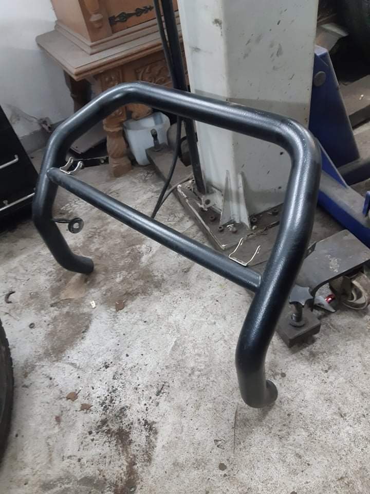 Czarna, metalowa konstrukcja rurowa, prawdopodobnie orurowanie ochronne do samochodu, leżąca na betonowej podłodze w warsztacie, widoczne ślady użytkowania i zabrudzenia.