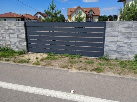 Nowoczesne ogrodzenie posesji z poziomych, szarych paneli, osadzone na słupkach z szarej kostki betonowej, widok z poziomu ulicy.