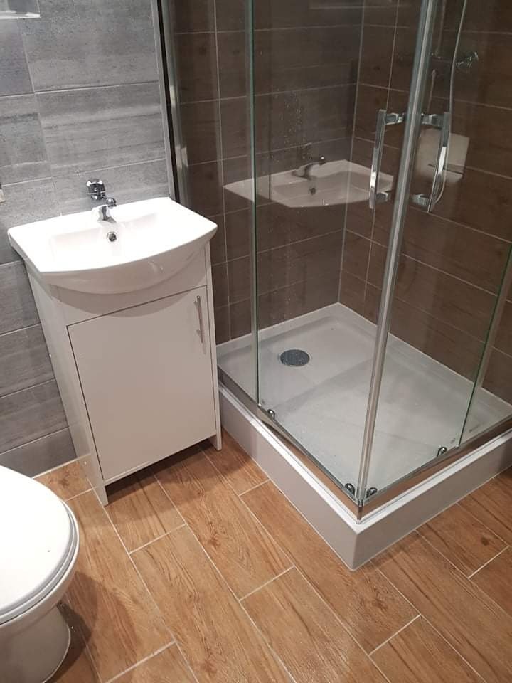 Nowoczesna łazienka z kabiną prysznicową, umywalką z szafką i drewnopodobnymi płytkami podłogowymi.