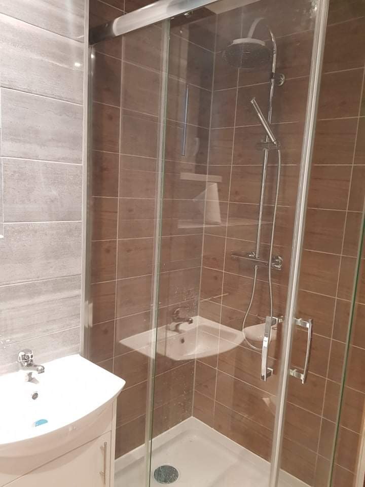 Nowoczesna łazienka z kabiną prysznicową ze szklanymi drzwiami przesuwnymi, umywalką nablatową na szafce i brązowymi płytkami ściennymi.