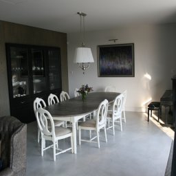 Sylwia Eymontt Architekt - Jasne wnętrze jadalni z długim, drewnianym stołem otoczonym białymi krzesłami, pod wiszącą lampą z abażurem, na tle ciemnej witryny i obrazu na ścianie, z widocznym fortepianem w rogu.