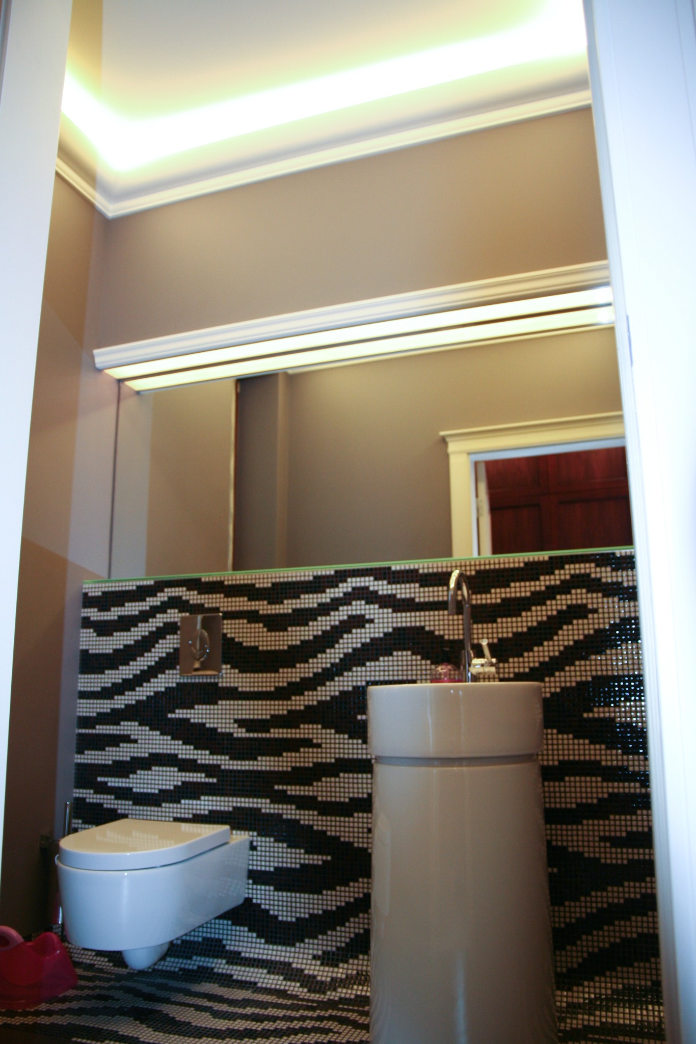 Nowoczesna łazienka z mozaiką w czarno-białe pasy zebry na ścianach i podłodze, z wiszącą toaletą i umywalką na postumencie, oświetleniem LED podsufitowym.